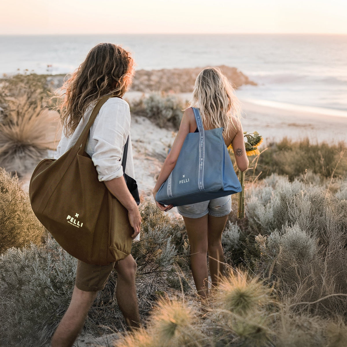 Two friends walking home over the dunes with Pelli beach bags